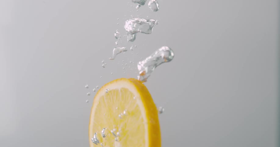 A lemon slice sinks into clear liquid and bubbles rise