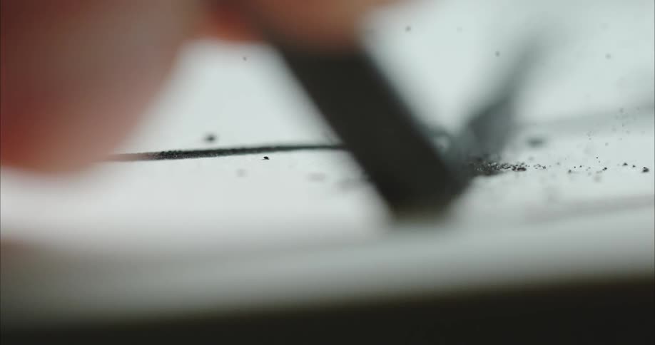 Thick black line being hand drawn with charcoal over rough paper
