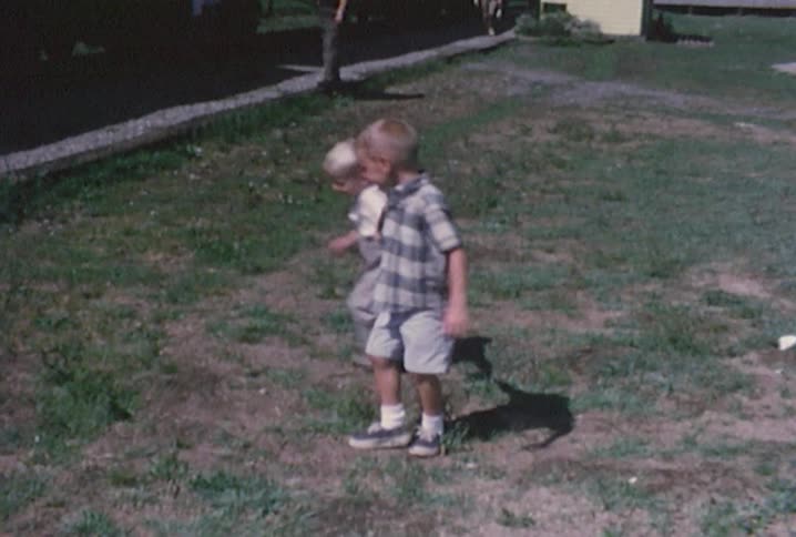 A young boy holds the hand of his younger brother as he runs around in a circle