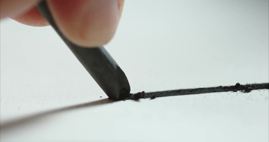 Bits of a charcoal stick flake off as a person uses it to draw a line