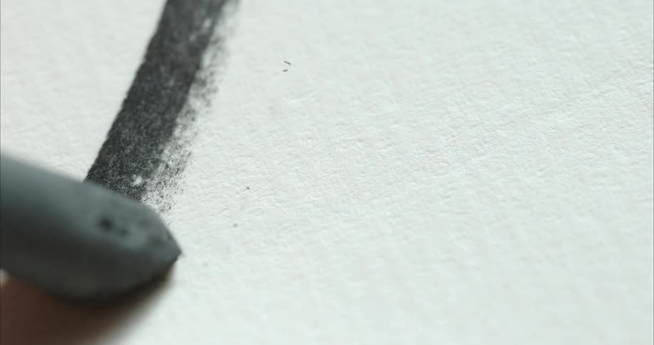 A person uses charcoal to draw a line on a white piece of paper