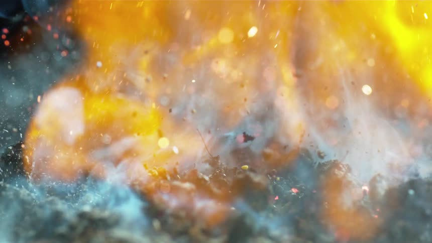 A pile of crumbled coal is shaken as a robust fire burns upon it and gives rise to embers and smoke