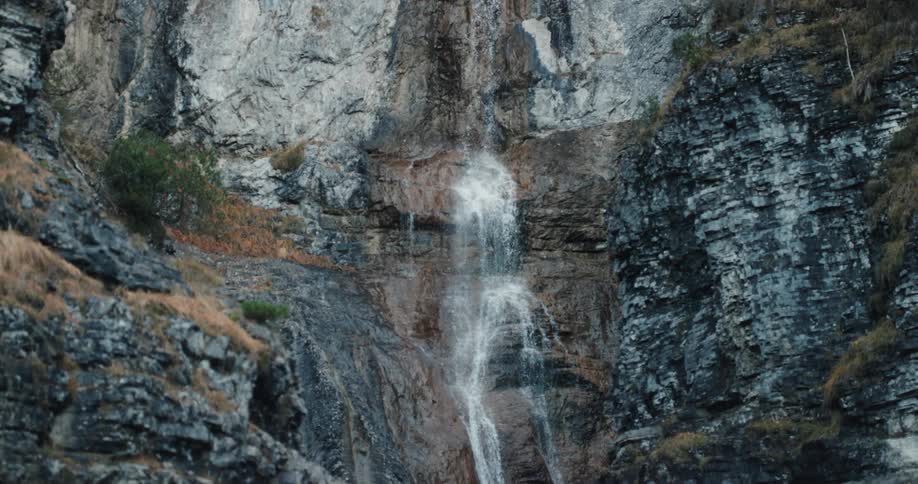 A large waterfall pours down a tall rock cliffside that is lined with trees