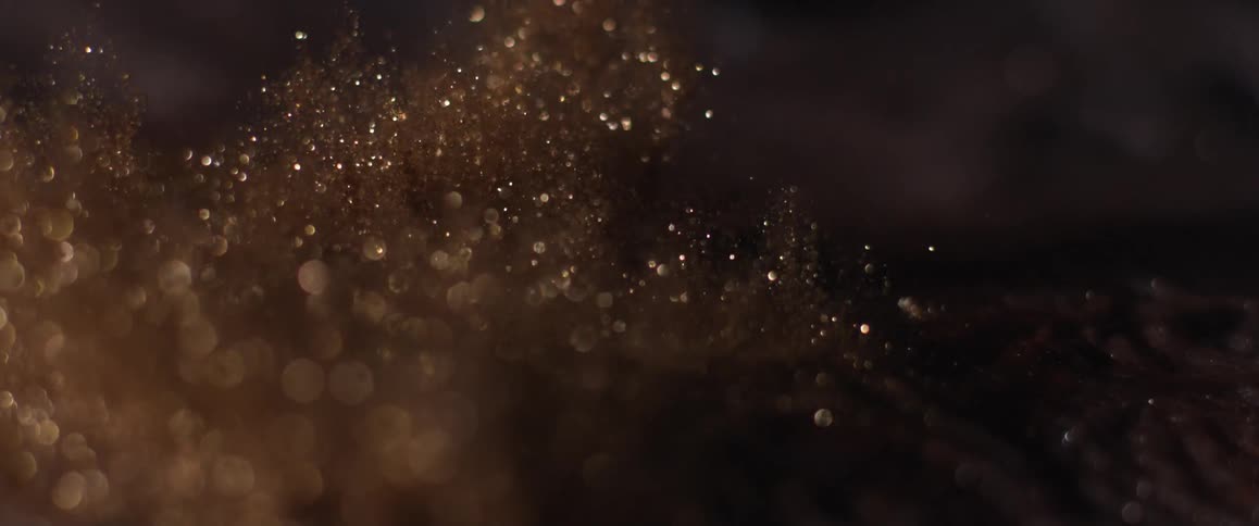 A pile of glitter golden particles are launched slightly upwards as if stuck from below