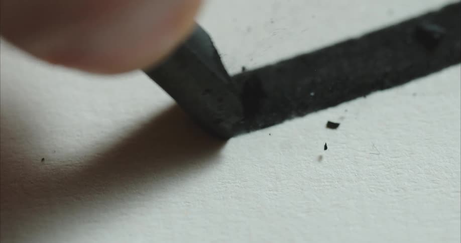 Thick black line being hand drawn with charcoal over rough paper