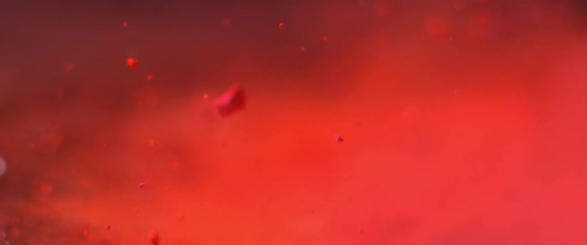 A blast of air launches small chunks of powder upwards from a glowing red background