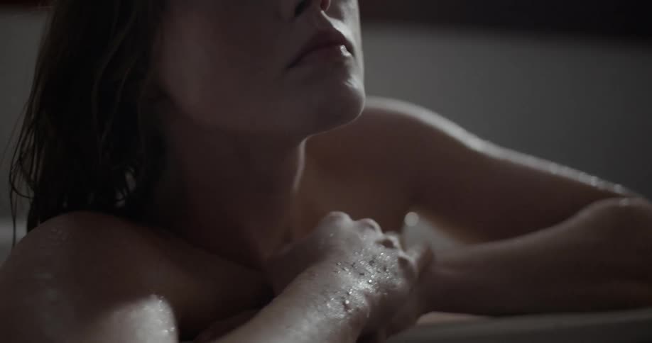 A woman sitting up in a bath tub with her arms resting on the tile edge