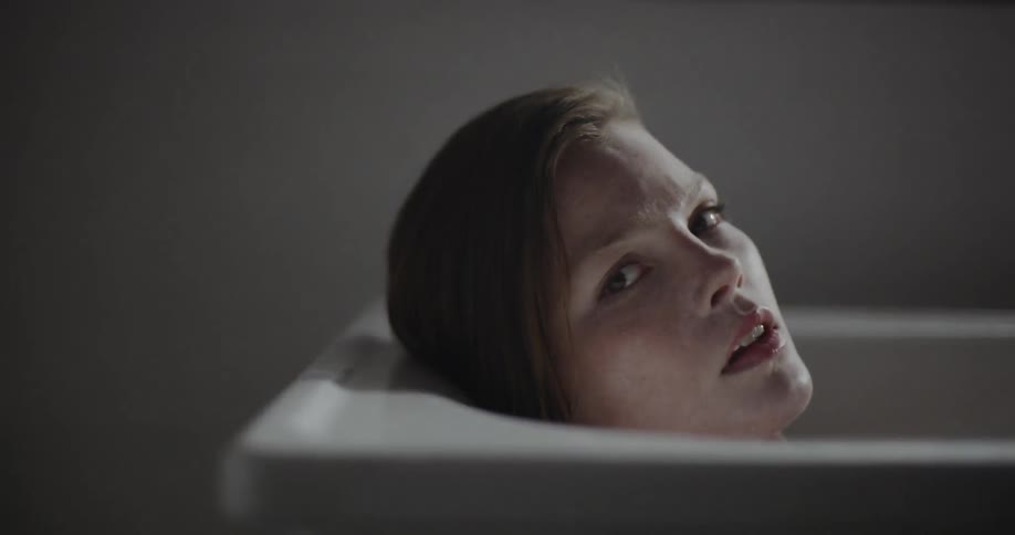 A young woman lays back into a bathtub and rests her head on the side of it