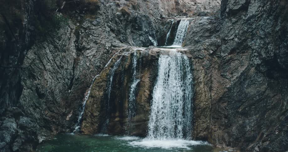 Water cascades down the rocky face of a waterfall and splashes down into the body of water below