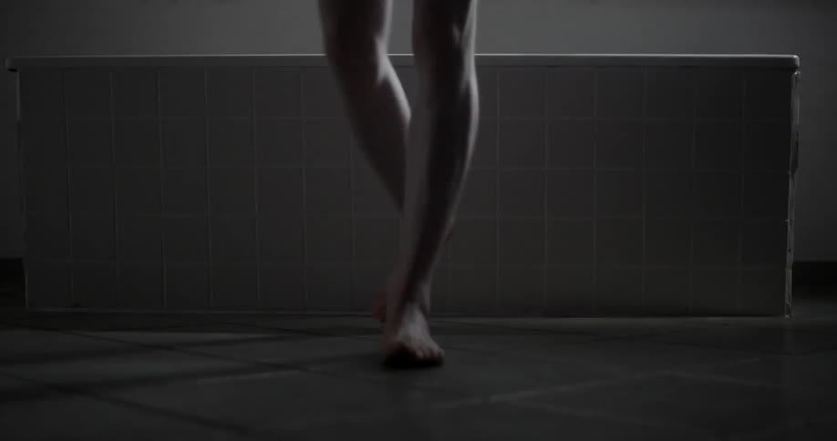 A female steps over the edge of a bathtub and walks away from it