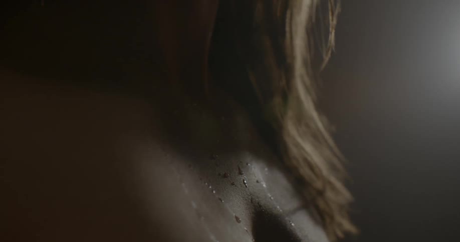 Drops of sweat on the bare chest of a woman standing on a dim lit room