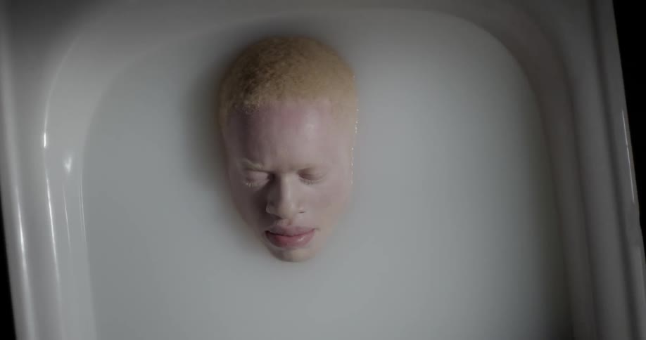 Man lays in a tub of white liquid with only his head visible