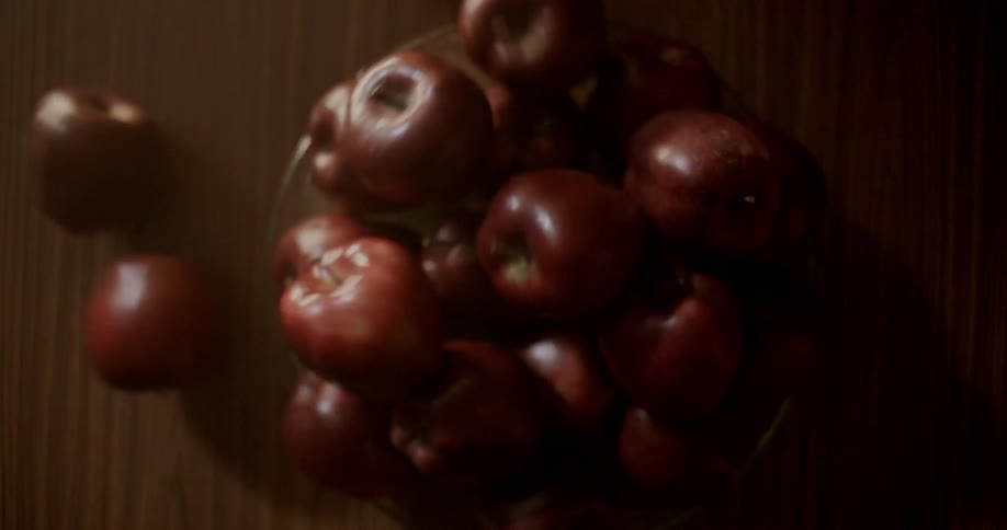 A pile of apples sits atop a table which is bumped from below and causes some apples to tumble