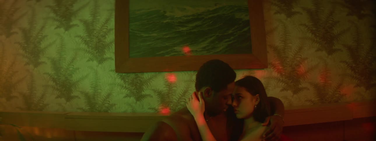 A man and woman hold each other close sitting in a dark room with disco ball lights