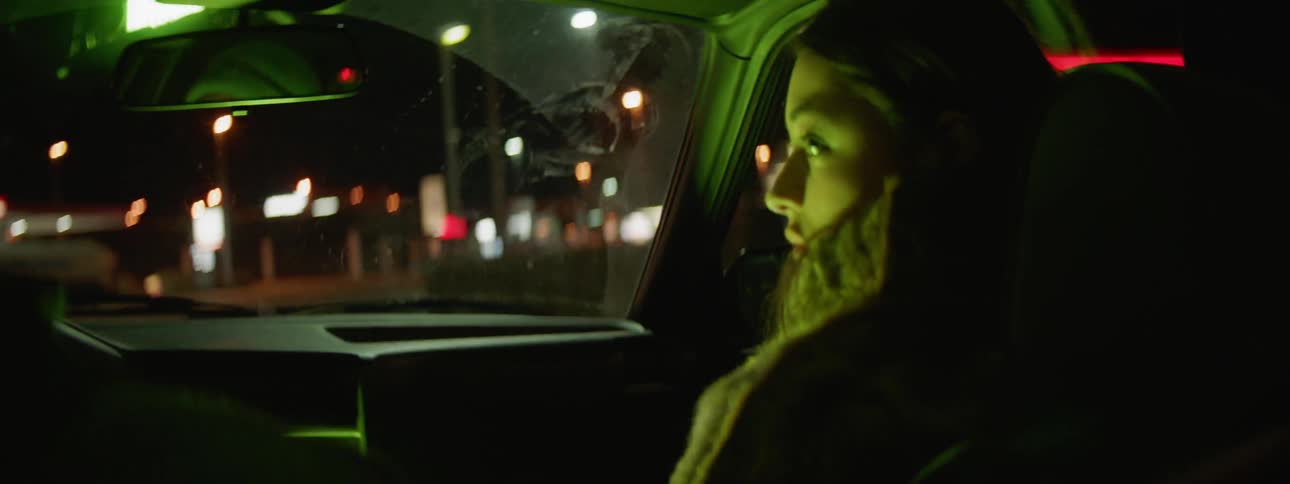 A young woman sits in the passenger seat of a car while looking at and talking to the male driver
