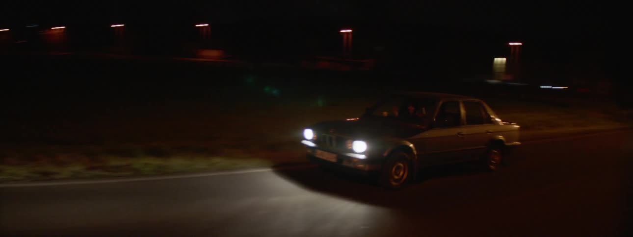 Car drives down empty road leading to city at night