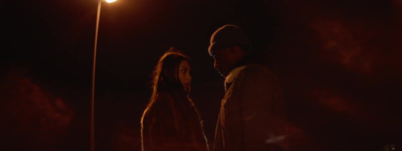 Man and woman stand close together underneath a street light at night and look very seriously into each others eyes