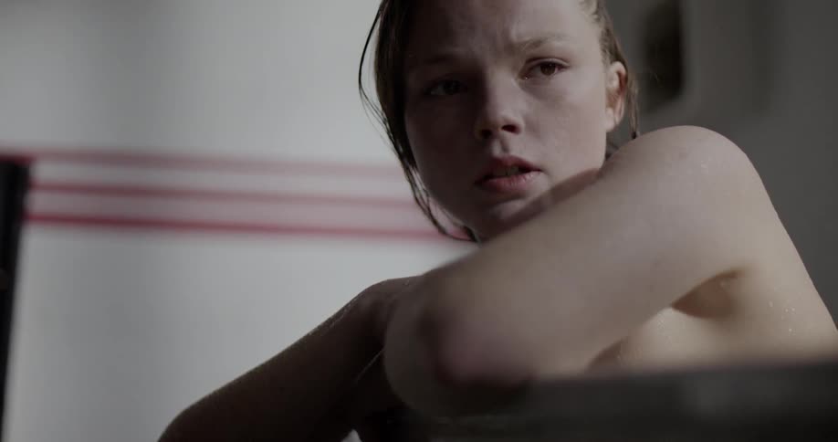 A young girls leans against the side of the bathtub she is in