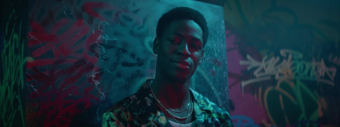A young black male stands inside of a club and smiles before standing up