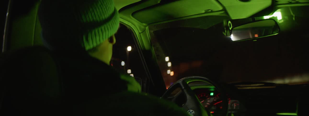 A male wearing a knit cap is driving a car looks to the right and then makes a lefthand turn