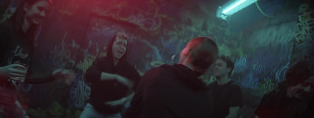 Several young people are all dancing in a club with graffiti covered walls and bright strobing lights