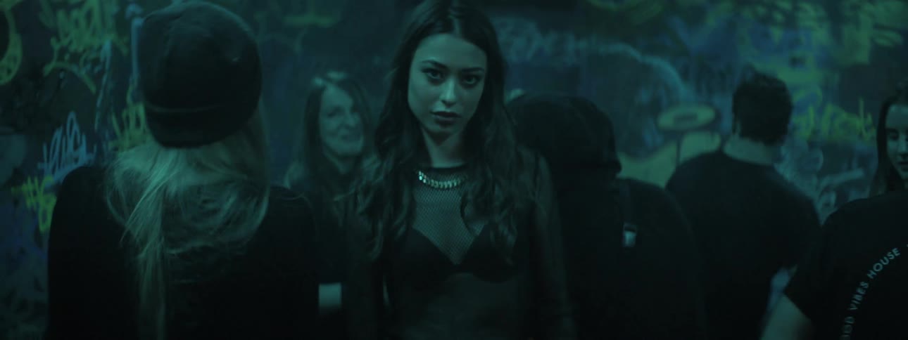 A woman walks through a dance club with people dancing around her