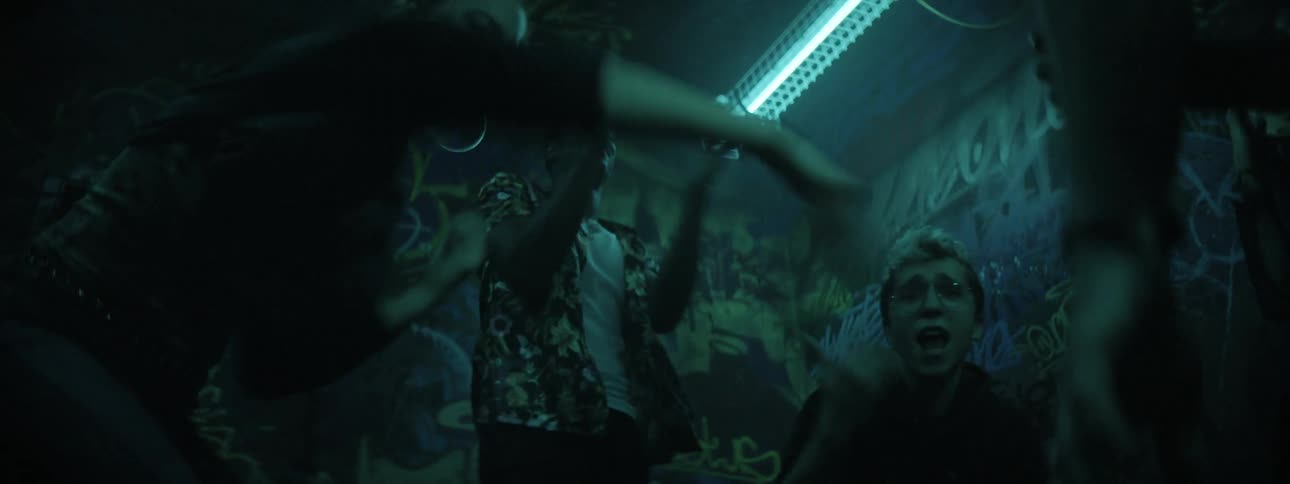 A group of people dancing in a graffiti covered room with strobe lights