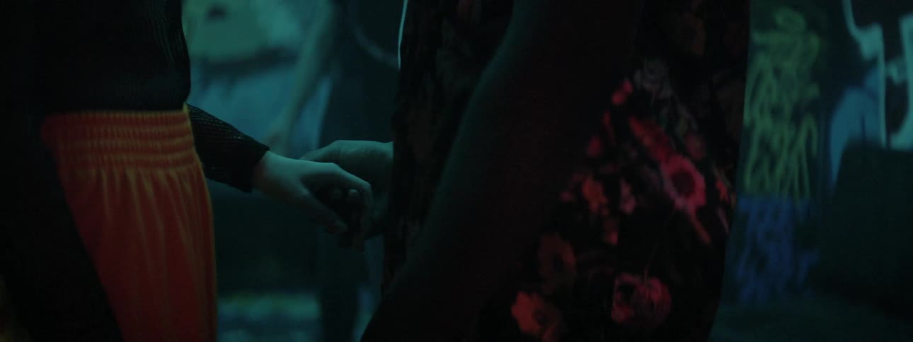A man walks through a night club and reaches for a womans hand and pulls her close