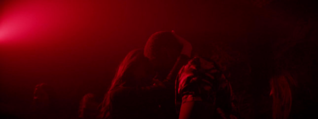 A male and female dance and kiss under flashing lights