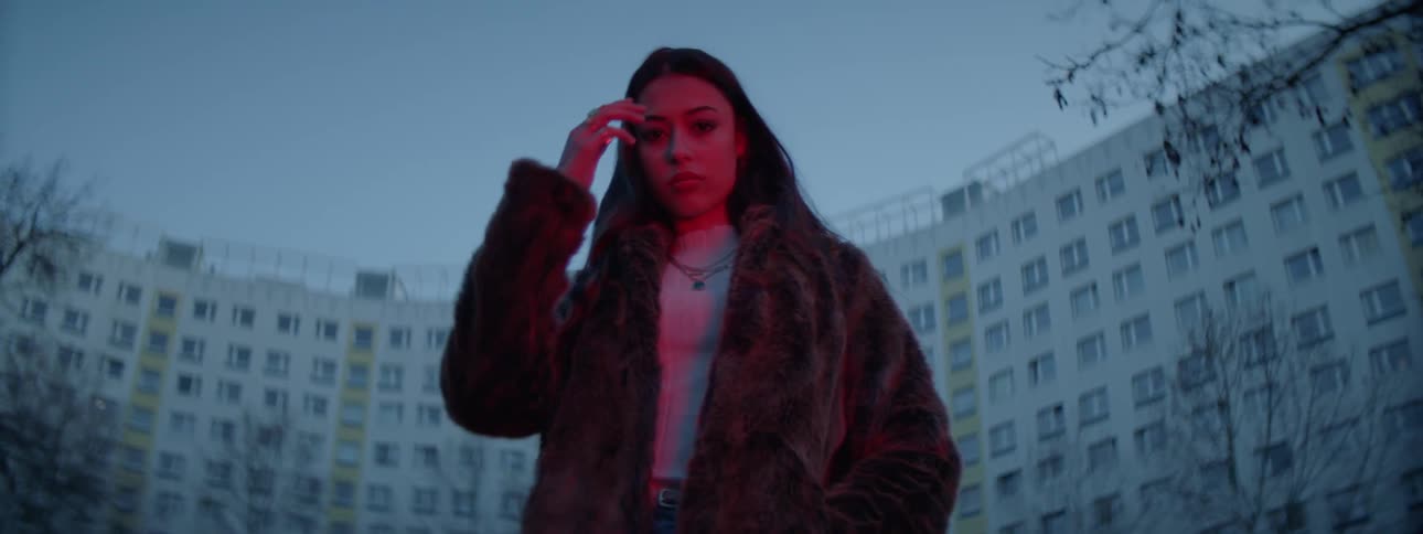 A woman stands outside a large apartment building and fixes her hair