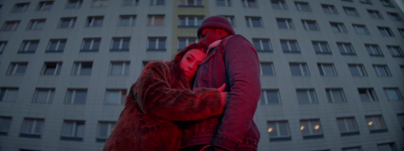 A woman holds on to a man and hugs him outside of an apartment building