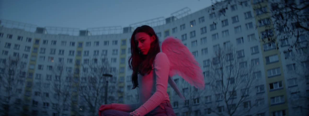 A woman with angel wings stooping down with buildings in the background