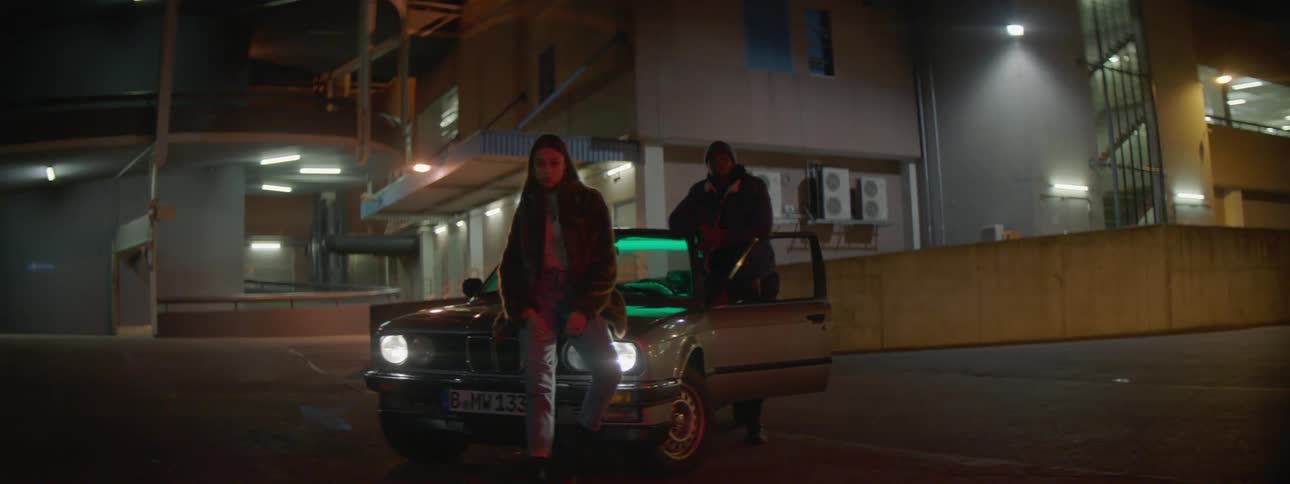 A woman sitting on the hood of a car with a man standing with the door open