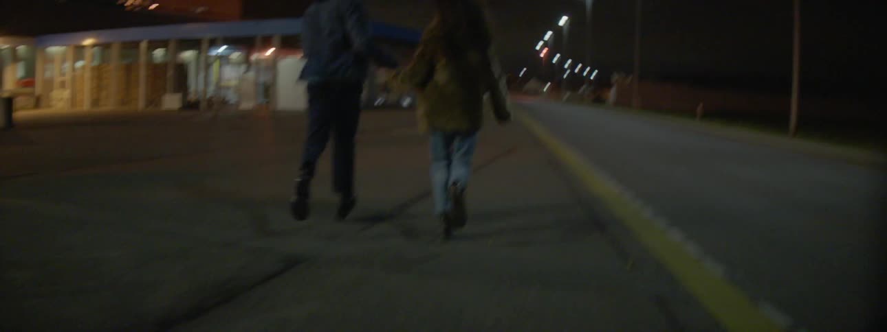 A man and woman hold hands while running down a street at night
