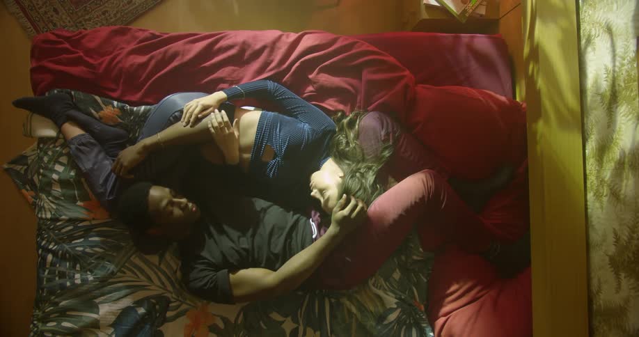 A man and woman lie in bed curled around each other and caressing