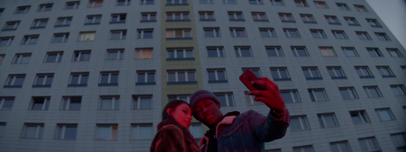 Black man and asian woman taking a selfie in front of a building
