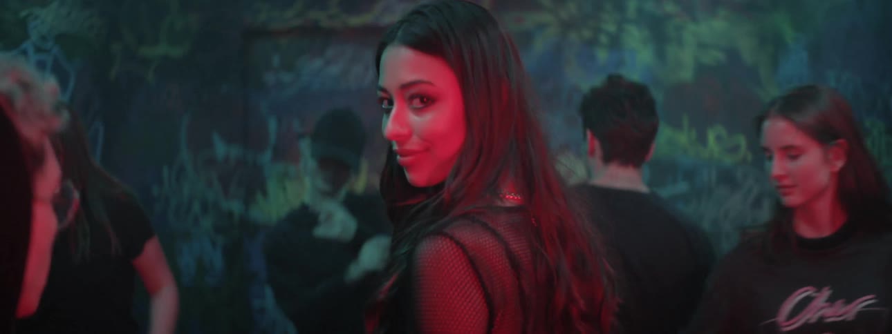 A woman walks through a graffiti covered room with strobe lights and dancers