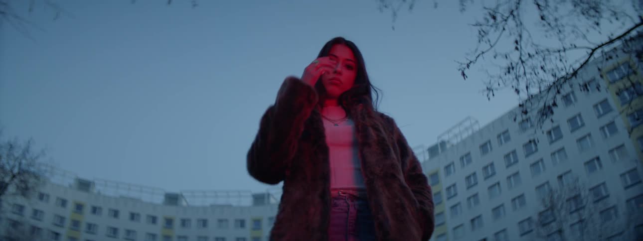 A woman in a winter coat posing in front of a large modern building