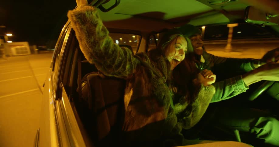 A man driving wildly through a parking lot as a woman laughs in the passenger seat