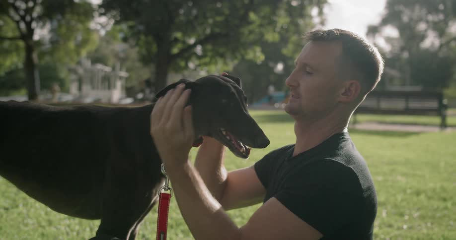A man is in a park with his dog which he is happily petting and rubbing