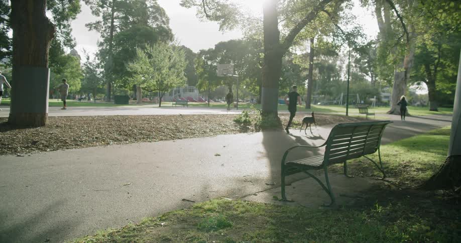 A park with a man running with his dog and a basketball court in the background