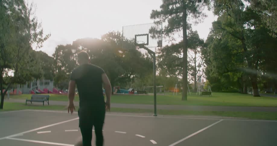 A young man dribbles a basketball and then runs and makes a shot