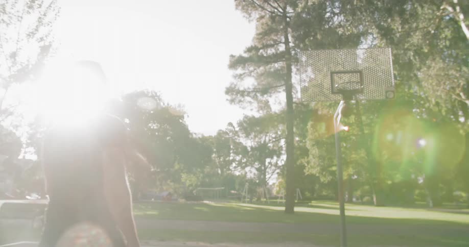 A tall man shoots a basketball and sinks his shot at an outdoor basketball court located in a park