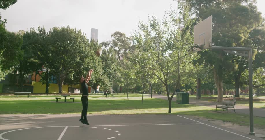 A man dribbling and shooting a basketball on a public court in a park