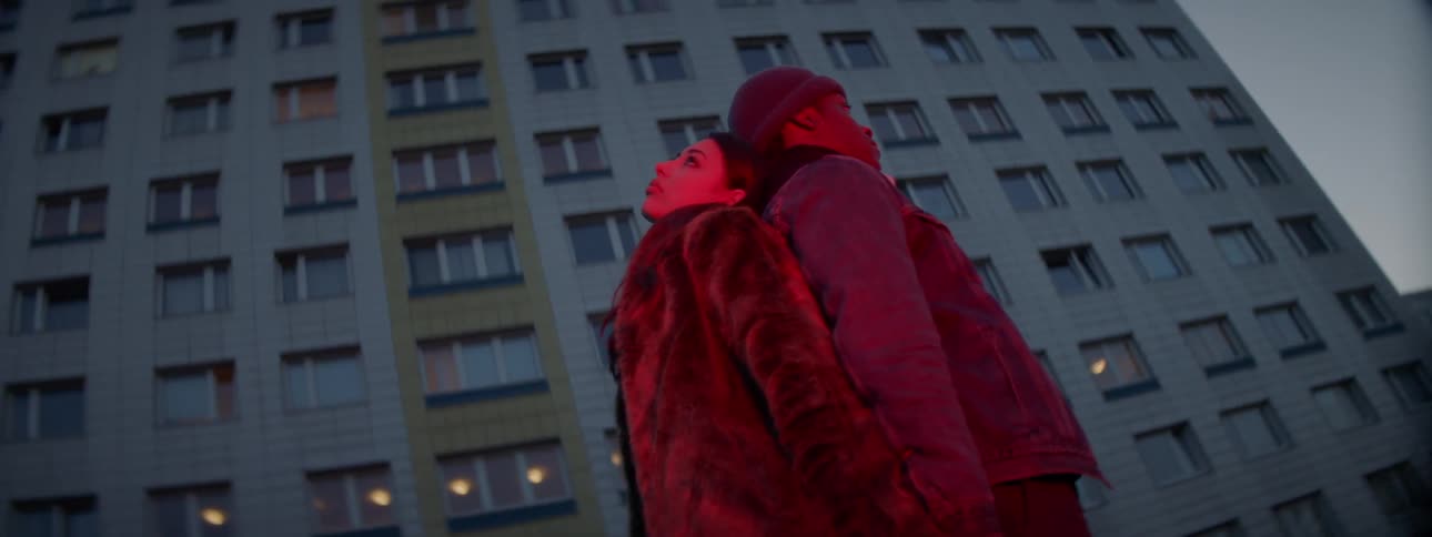 A man and woman standing back to back holding hands in front of an apartment building