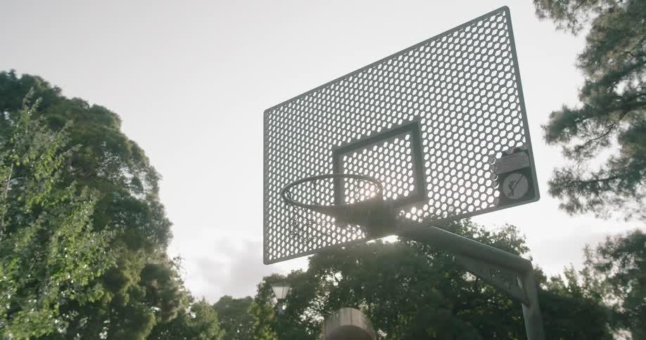 Basketball falls through hoop without touching backboard outdoors during the day