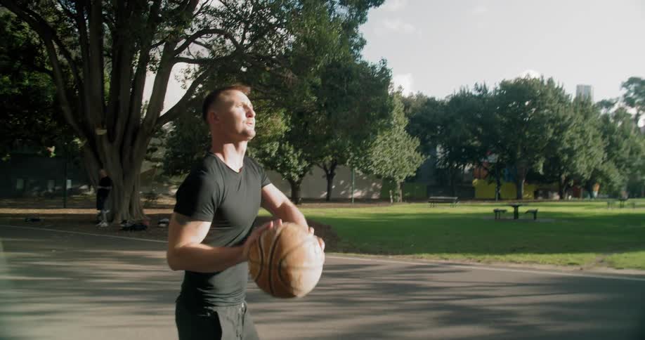 A man on a public basketball court dribbling a basketball before shooting it
