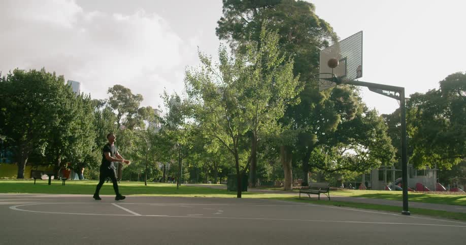 A tall male takes a practice shot and misses while at an outdoor basketball court located in a public park