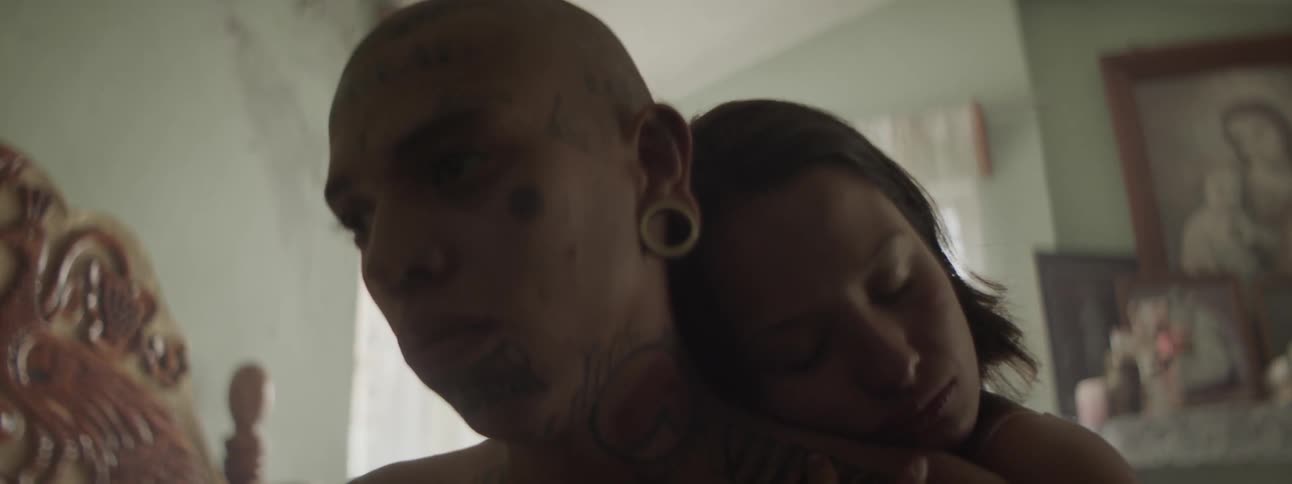 A man sitting on a bad as a woman embraces him from behind