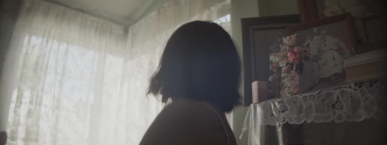 A woman looking at a curtained window inside a house